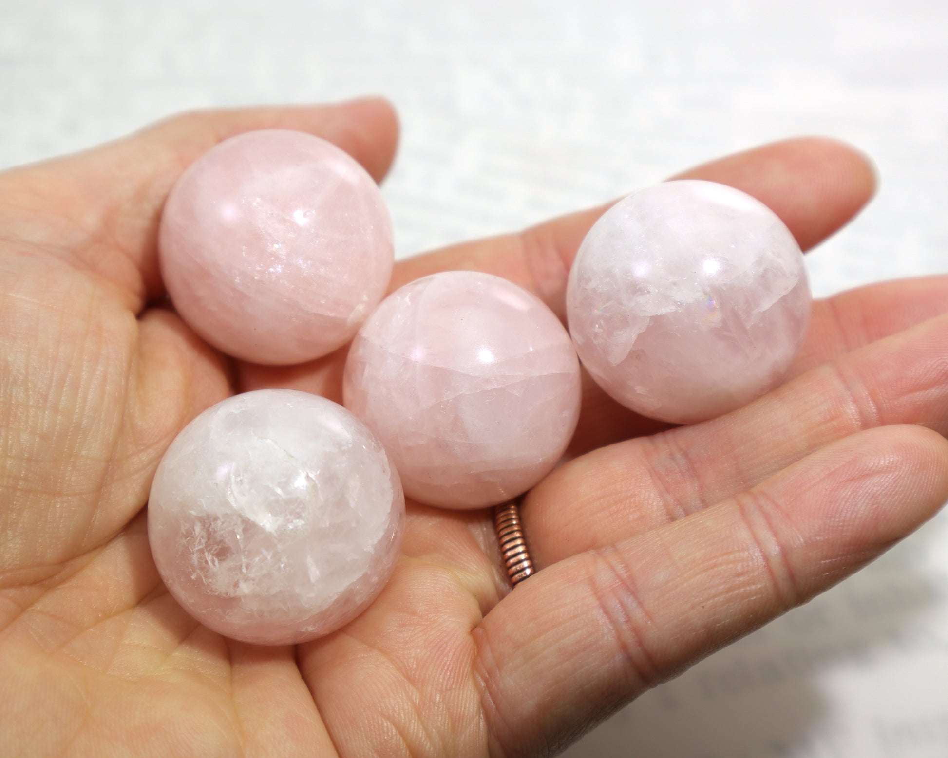Hand holding four pink rose quartz crystal balls against a white background