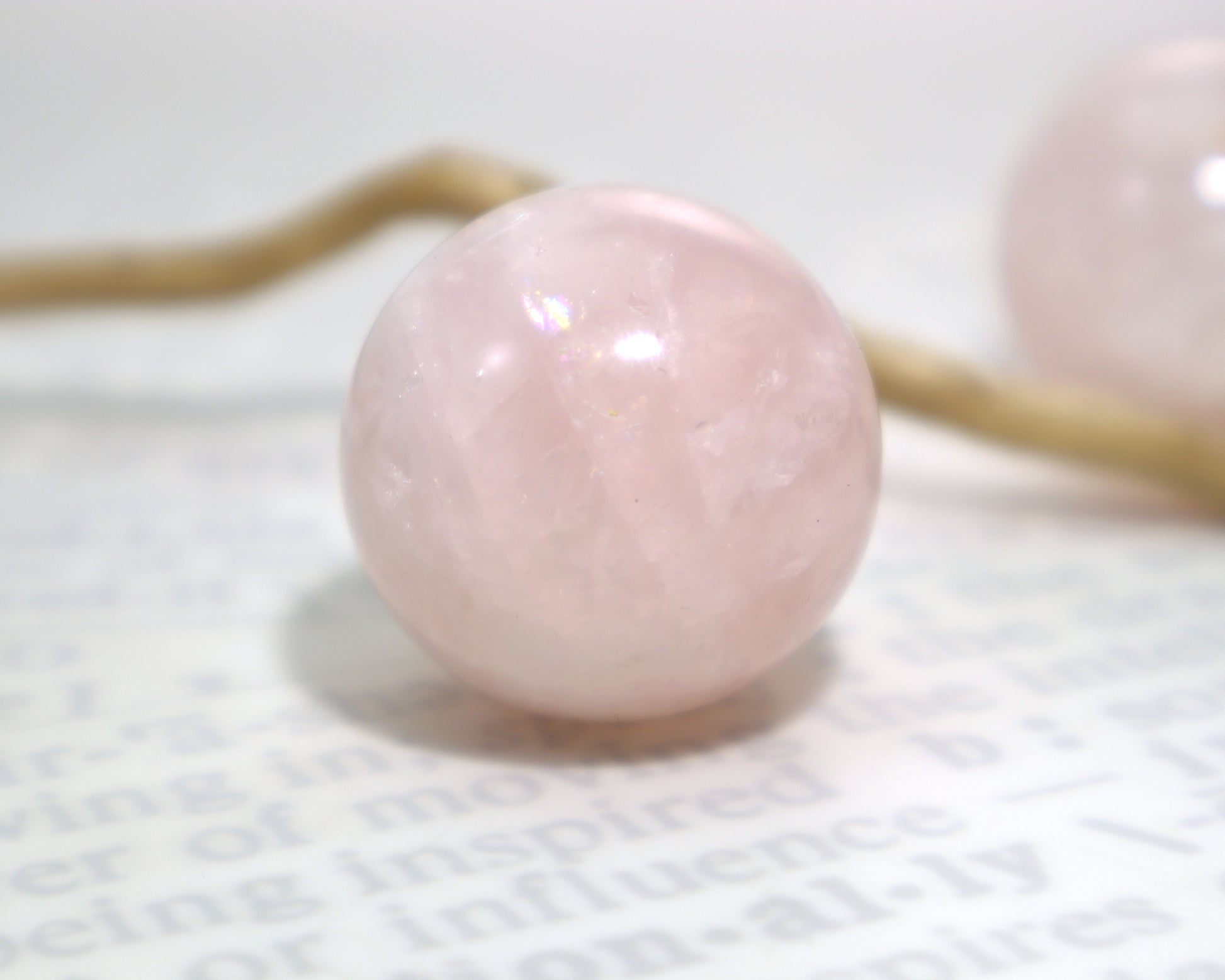 28mm rose quartz sphere with soft pink and white tones on a textured white surface with a piece of driftwood in the background