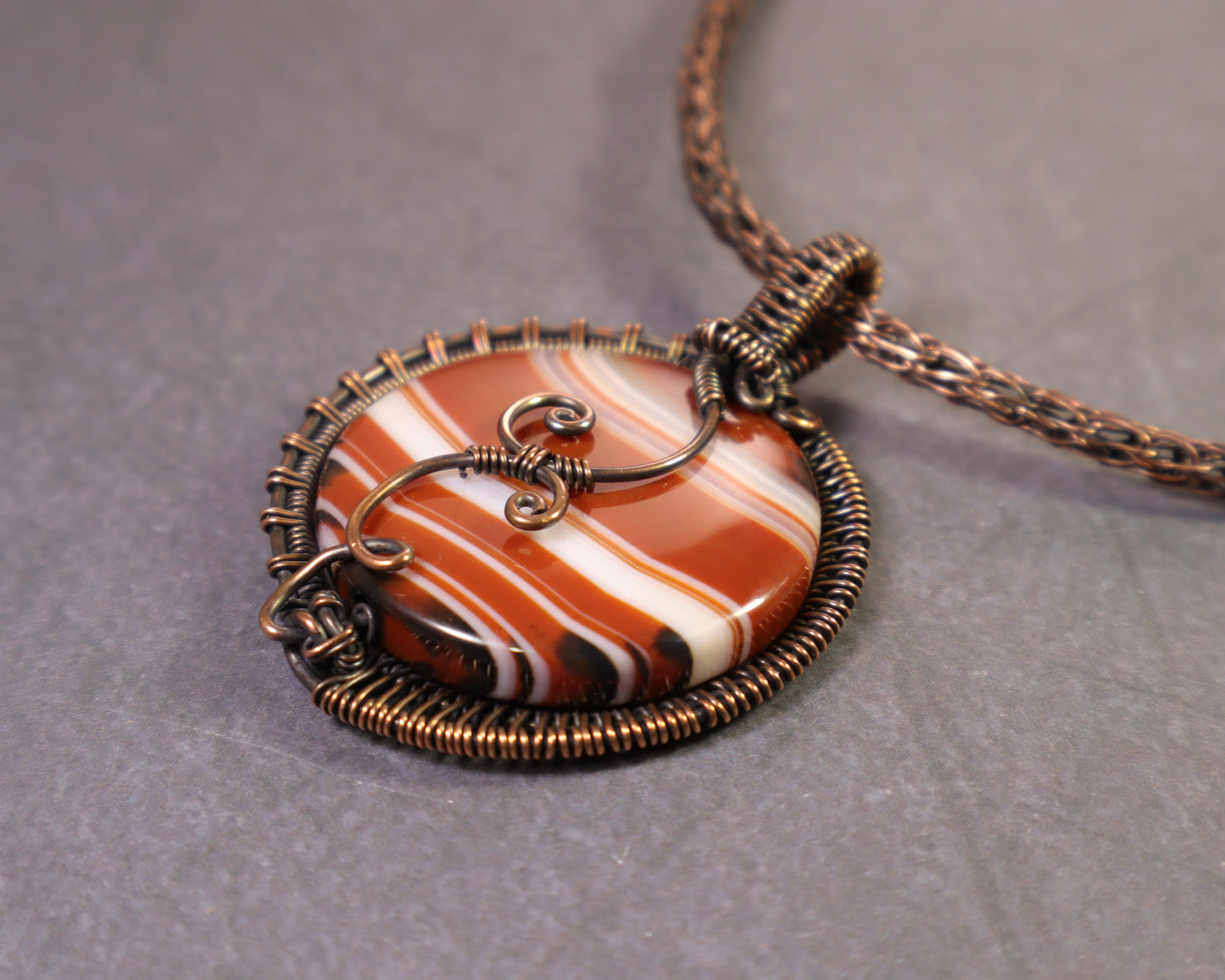 Reversible sardonyx pendant featuring decorative copper swirl details
