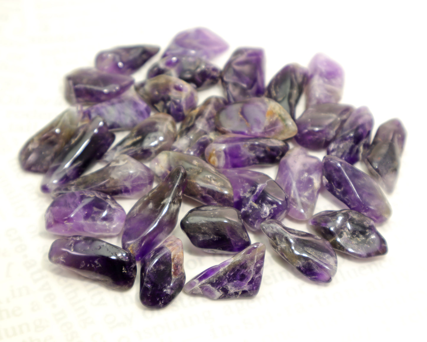 Assorted deep purple amethyst tumbled stones with zoning on white background