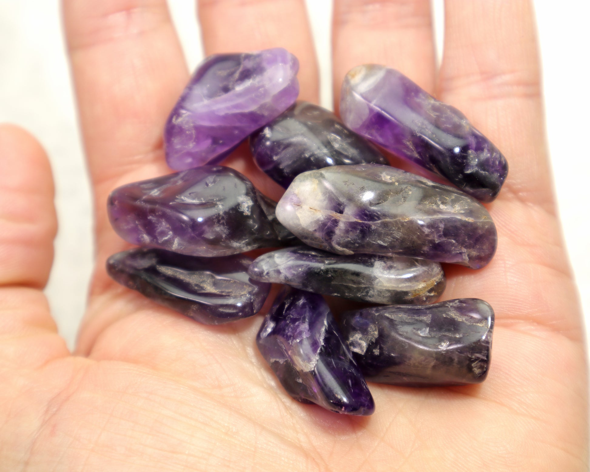 Hand holding polished dark purple amethyst crystals, one chevron