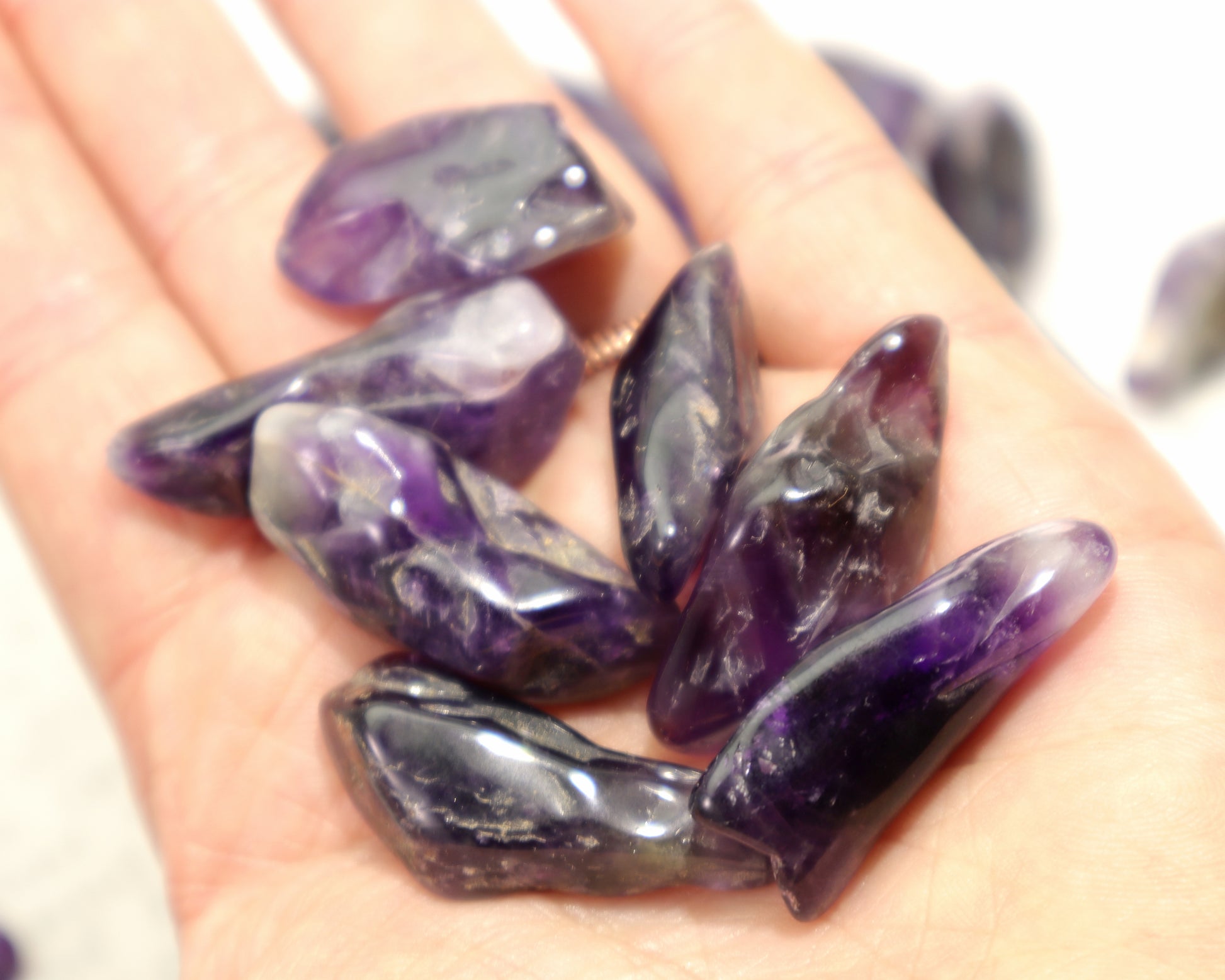 Hand holding deep purple amethyst tumbled stones with smoky zoning