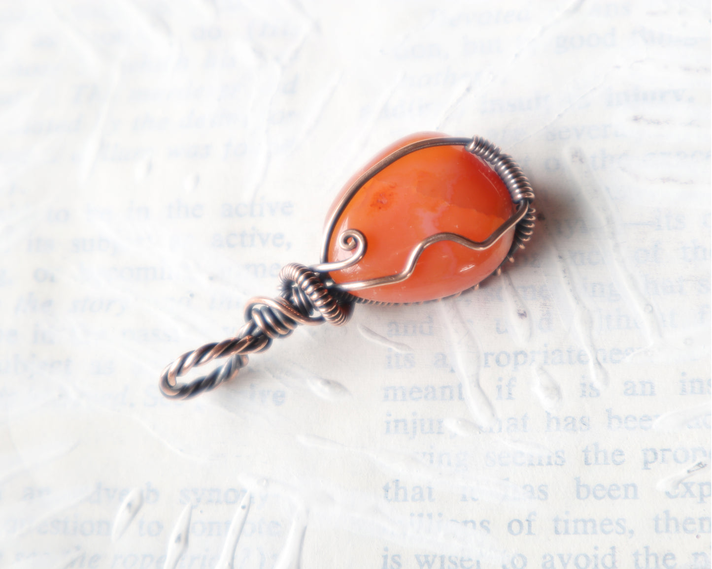 Warm orange carnelian gemstone pendant with decorative copper swirls